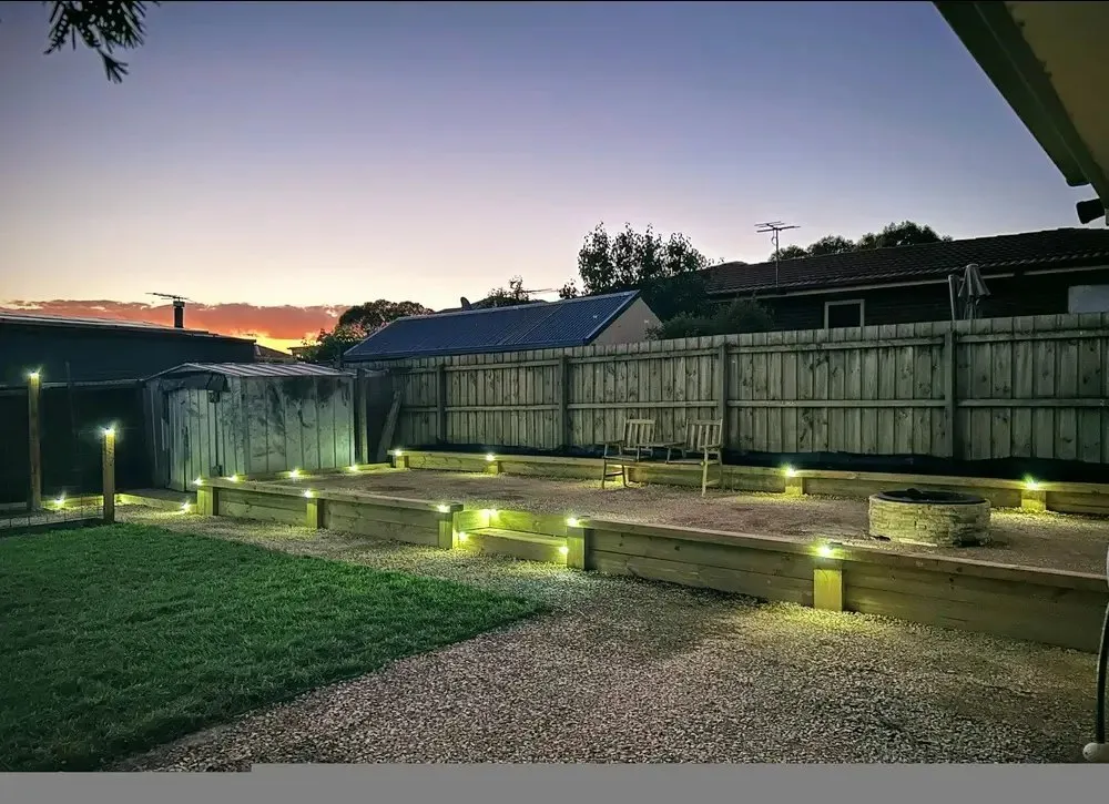 Backyard at sunset with timber sleeper retaining walls, integrated garden lighting, gravel and lawn