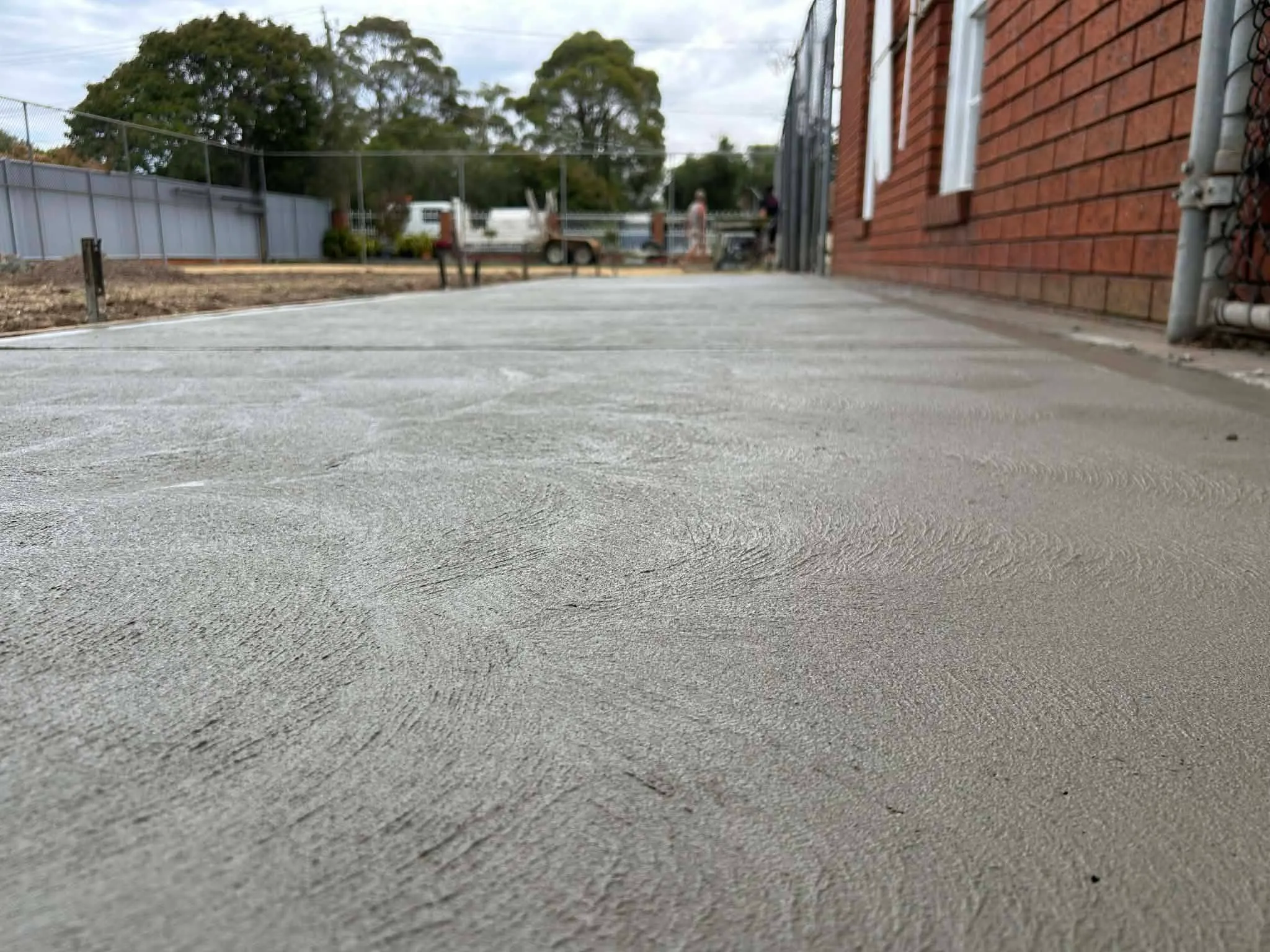 Low-angle view of a new broom-finish concrete path beside a brick building in Geelong
