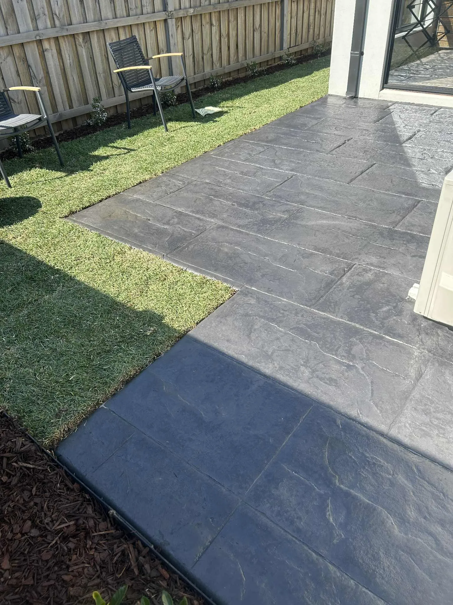 Charcoal slate-pattern stamped concrete patio meeting freshly laid turf in a fenced backyard