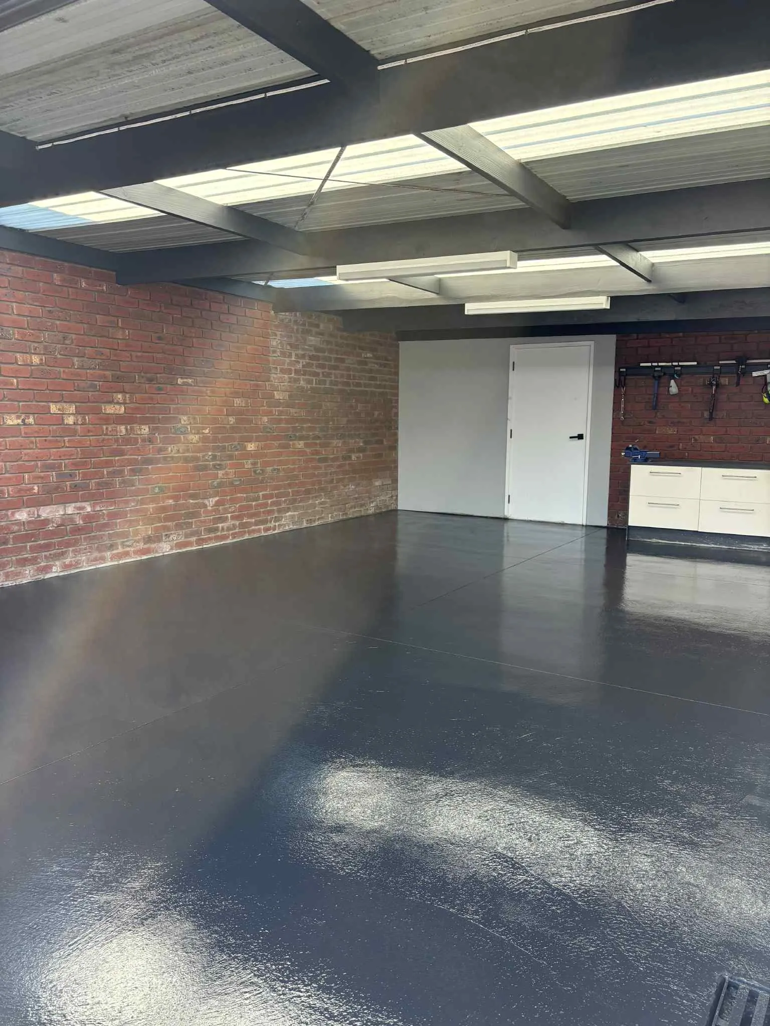 Glossy charcoal coloured and sealed concrete floor inside a large brick garage workshop