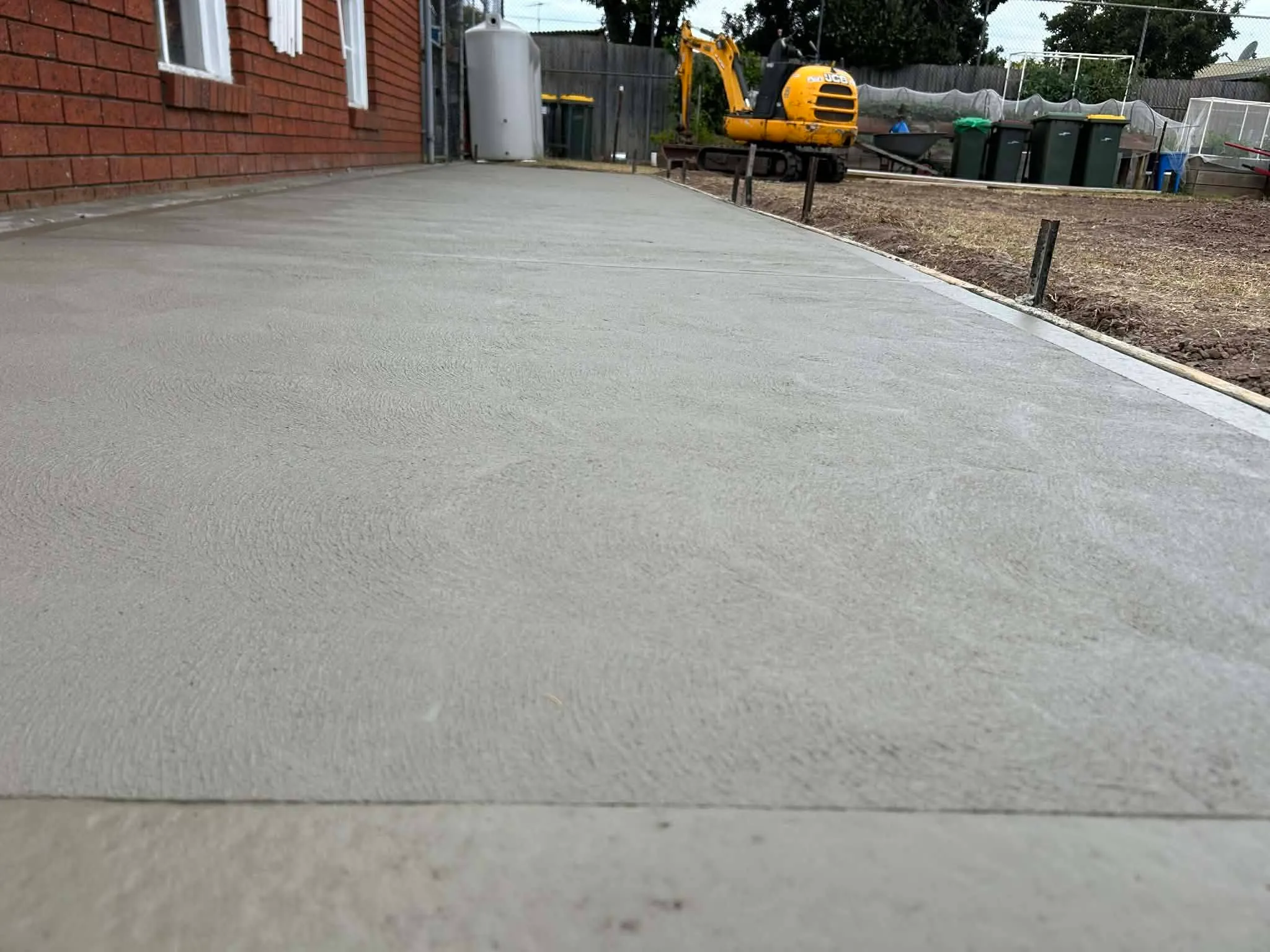 Freshly finished broom-finish concrete driveway running alongside a brick home in Geelong