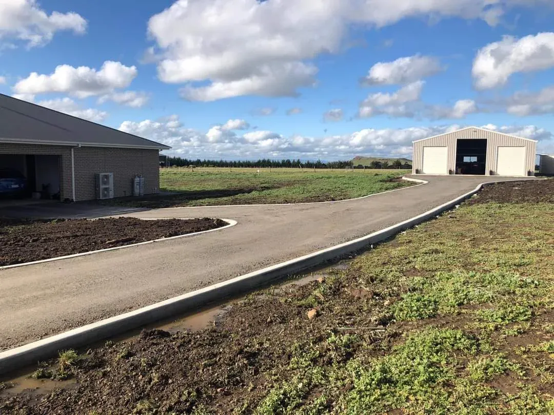 Long concrete driveway curving up to sheds on a rural property under a blue sky