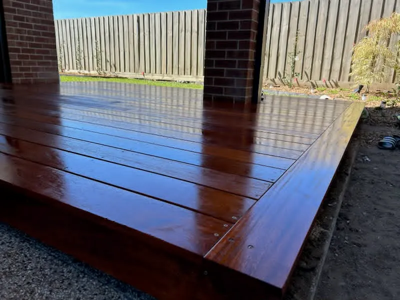 Freshly oiled merbau timber deck against brick pillars, with a new timber fence and lawn behind