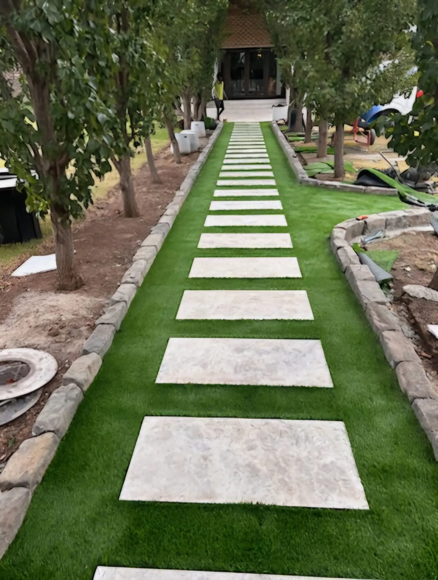 Large paver stepping-stones set in lush turf forming a path through a tree-lined garden entrance