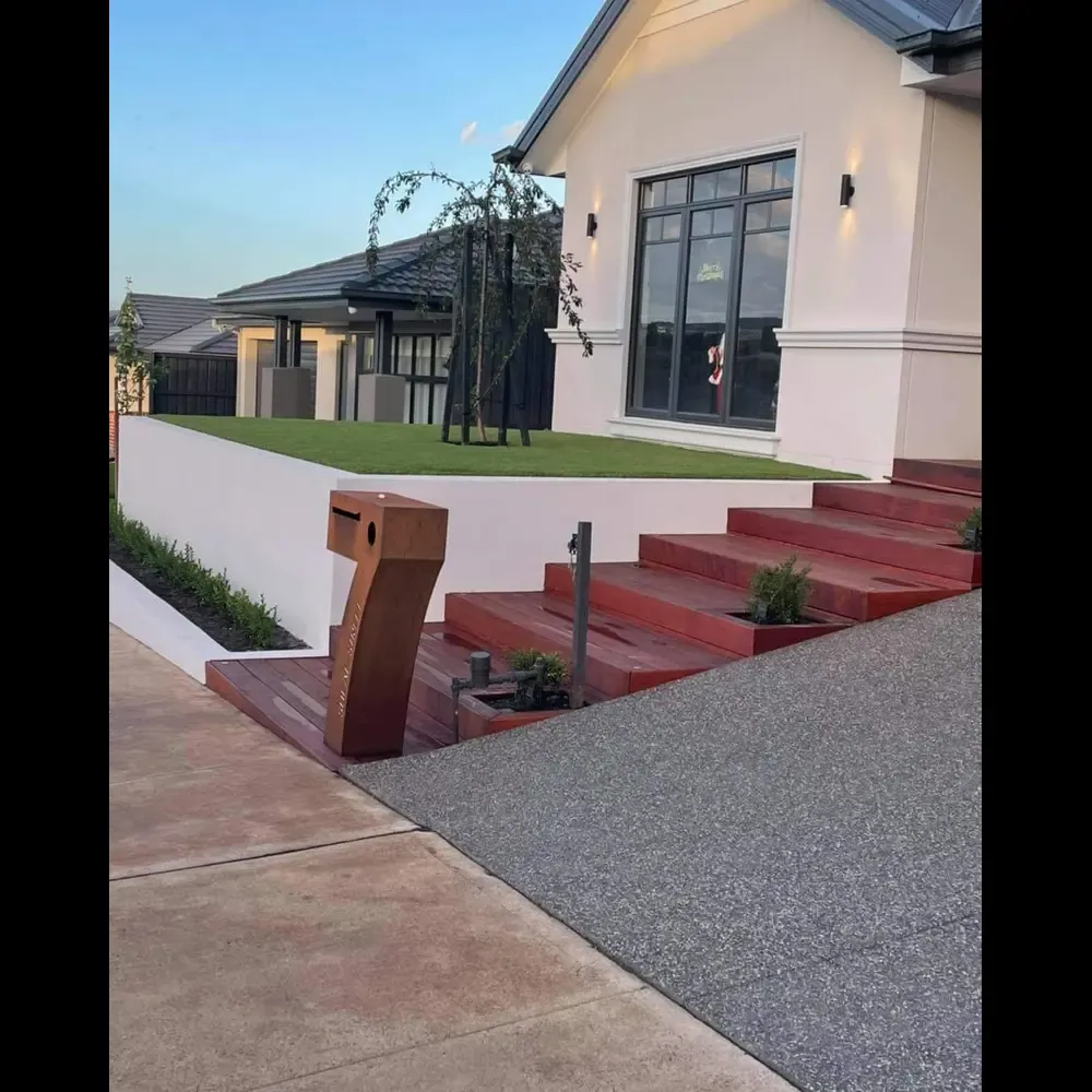 Modern home frontage with a rendered retaining wall, timber steps, exposed-aggregate driveway, turf lawn and corten steel letterbox