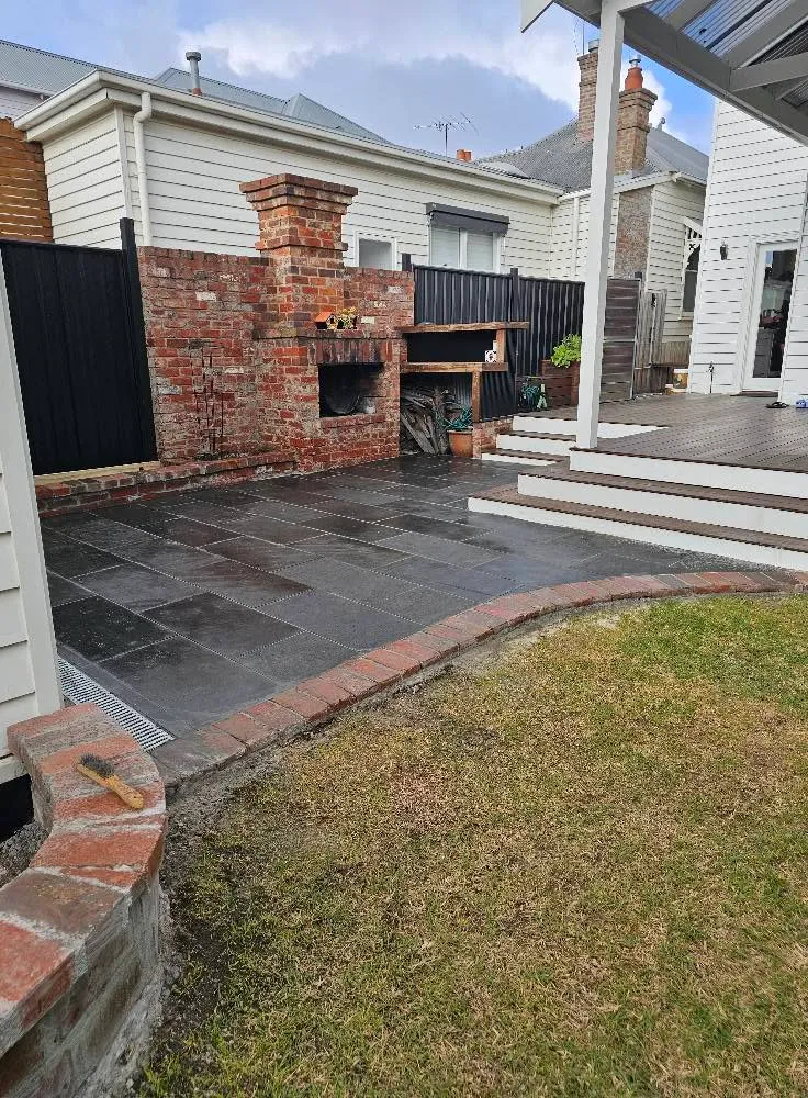 Slate-paved courtyard with a rendered brick wood-fired oven, brick retaining edge, timber deck and lawn