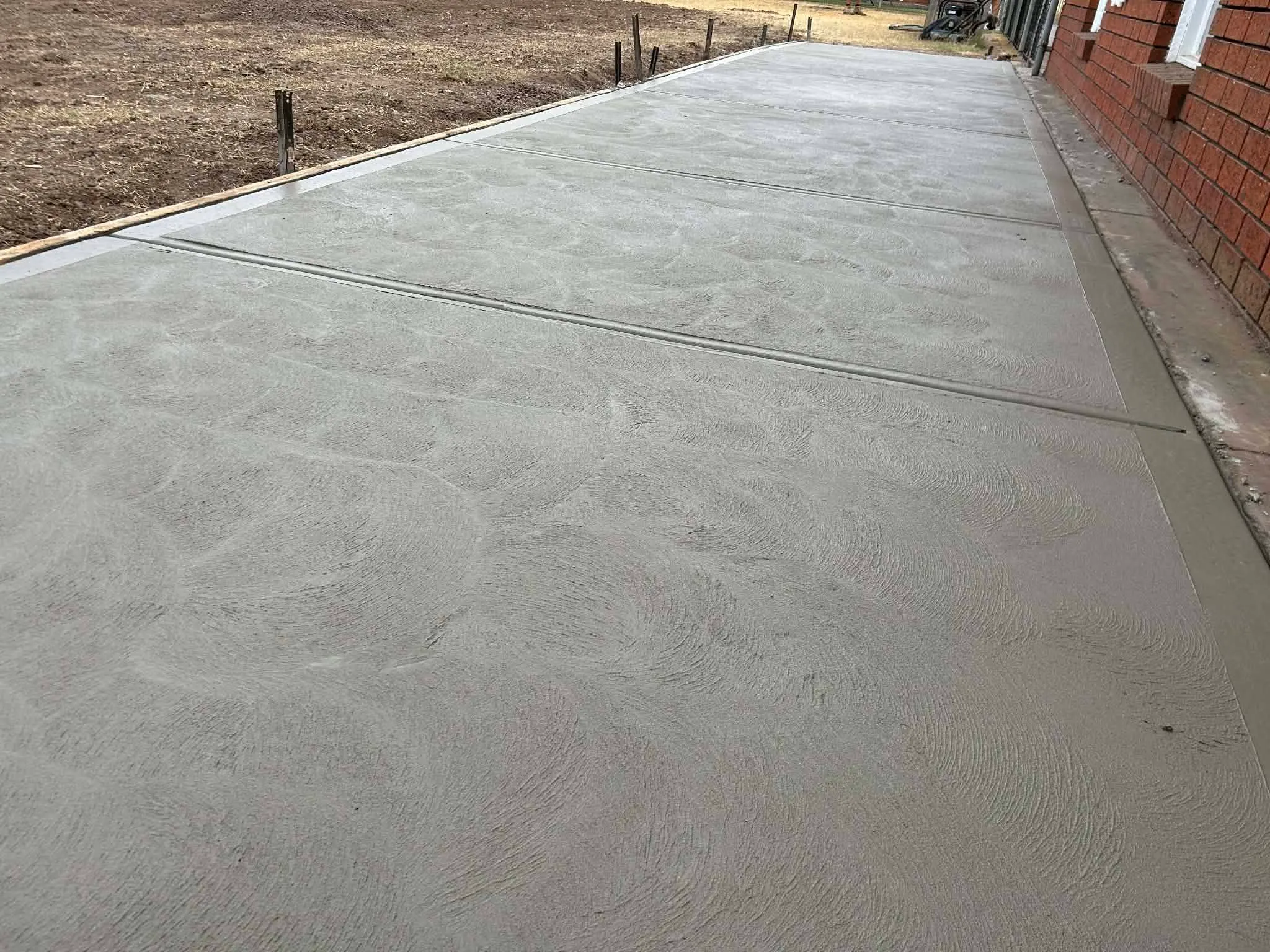 Freshly poured concrete driveway with a decorative swirl finish beside a brick home
