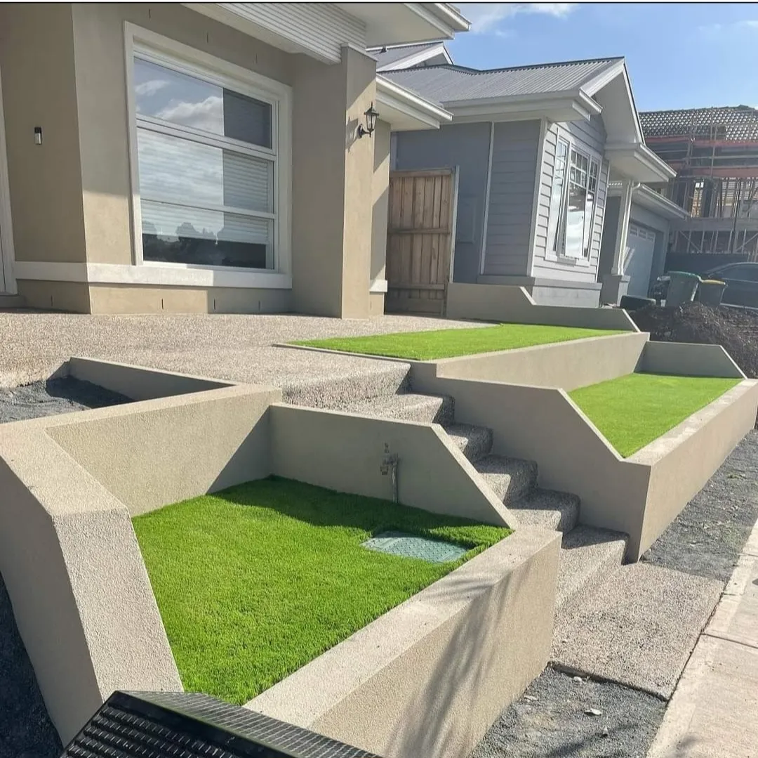 Tiered rendered planter walls with synthetic turf and exposed-aggregate surrounds at a modern home frontage