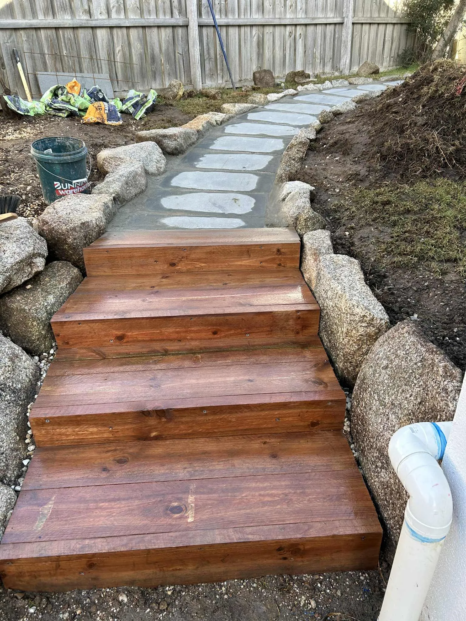 Timber sleeper steps and a stepping-stone path bordered by granite boulders during a garden build